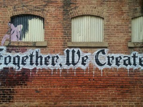 Eine Steinmauer mit einem Graffiti, was in stilisierten, serifen Lettern besagt "Together we create!"